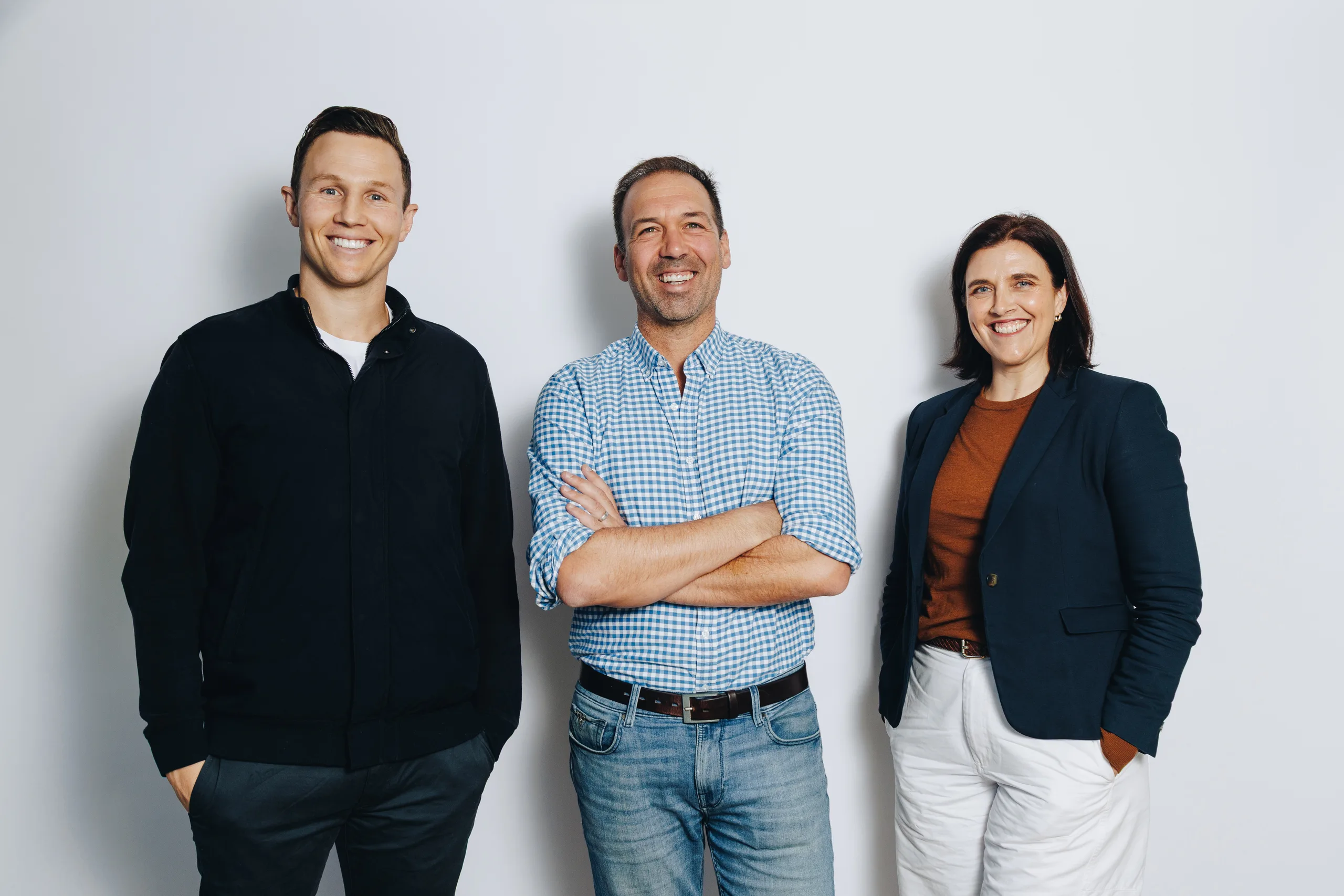 Three members of Jem's leadership team standing together, smiling, against a pale grey studio backdrop.