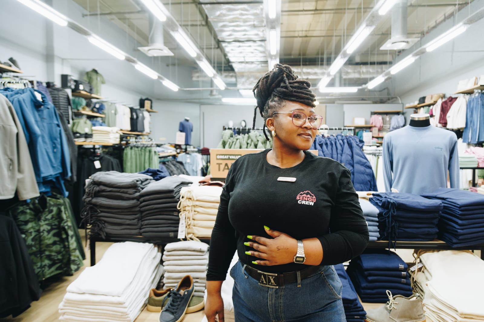 A Senqu Crew retail assistant standing among folded stock on a clothing shop floor